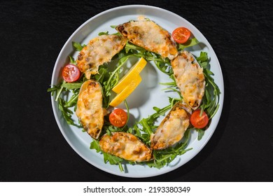 Cooked Oysters With Lemon, Tomato And Arugula On A White Plate On A Black Stone Background