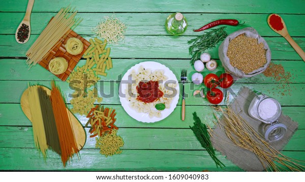 Cooked pasta on plate with tomato sauce. Top\
View.\
\
Demonstration of cooked bows pasta and dry pasta. Green\
table is divided into many types of dry pasta on the left side and\
vegetables on the right.