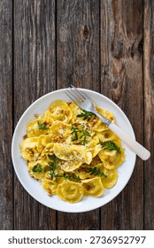 Cooked ravioli with pine nuts, rocket leaves and grated parmesan cheese on wooden table. Top view