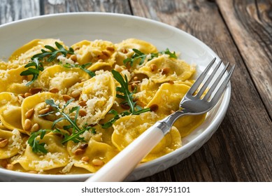 Cooked ravioli with pine nuts, rocket leaves and grated parmesan cheese on wooden table
