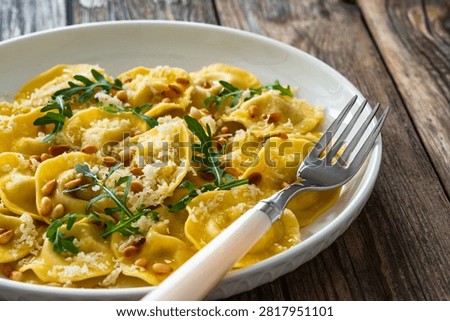 Cooked ravioli with pine nuts, rocket leaves and grated parmesan cheese on wooden table
