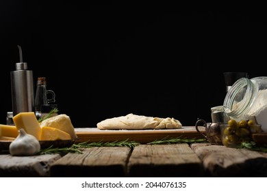 Cooked Raw Dough On A Wooden Cutting Board, Ingredients Next To It On A Wooden Table. Cooking Pasta, Pizza, Pie, Bread, Focaccia. Black Background. Wooden Texture. There Are No People In The Photo.