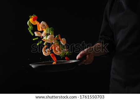 Cooked seafood, vegetables with shrimps are fried in a pan, frozen in motion, on a black background, restaurant menu