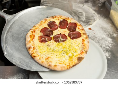 Cooked Truffle oil and Italian Dry-Cured Beef pizza on a metal pizza peel in table at a pizzeria.