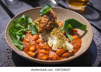 A Cooked White Fish Fillet Served On Beans In A Tomato Sauce With Green Leaves