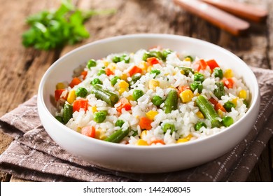 Cooked white rice mixed with colorful vegetables (onion, carrot, green peas, corn, green beans) in white bowl (Selective Focus, Focus in the middle of the dish)
