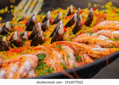 Cooked yellow paella with shrimp, mussel, rice, spice, saffron in huge paella pan at summer outdoor food market: close up. Spanish cuisine, seafood, gastronomy, street food concept