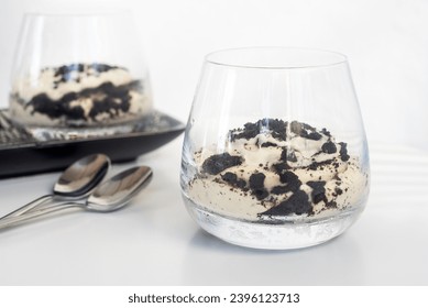 cookie and cream cheesecake in a short glass with spoon on white table.