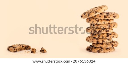 Cookie day banner with delicious freshly baked chocolate chip cookies in a tall stack, next to a partially eaten one with crumbs isolated on caramel beige background with copy space for text