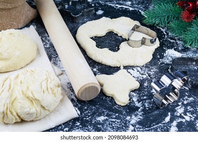 Cookie Dough On A Dark Table Strewn With Flour. Cookie Cutters, Rolling Pin, Dough Pieces In The Background. A Sprig Of Blue Spruce On The Table