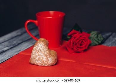 Cookie heart on a red napkin, red rose and mug