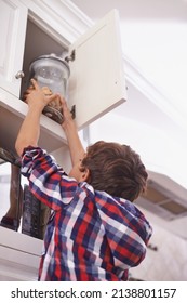 Cookie Time. A Young Boy Reaching For A Cookie Jar In The Top Kitchen Cupboard.