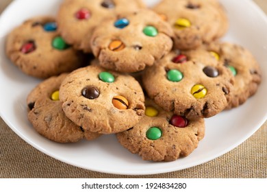 Cookies with colorfu M and Ms chocolates close-up on a white ceramic plate. Low depth of field, blurred background.