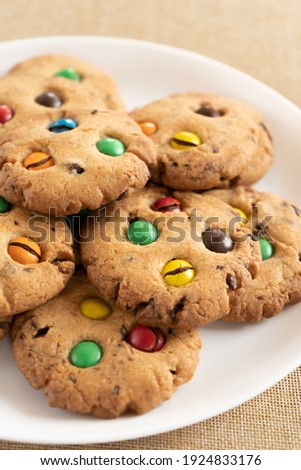 Cookies with colorful MMs chocolates close-up on a white ceramic plate. Low depth of field, blurred background.