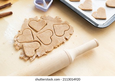 Cookies Cut Out In The Shape Of A Heart With A Rolling Pin On A Wooden Background. The Process Of Making Holiday Cookies For Valentine's Day. Home Baking With Love. Family Care Concept.