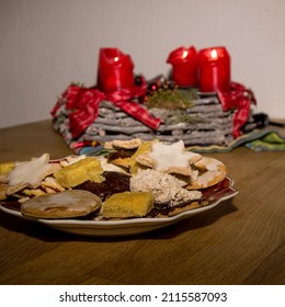 Cookies Lie On A Table In Front Of A Christmas Wrath With Candles Lit.