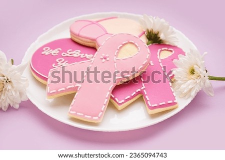 Cookies with pink ribbons, chrysanthemum flowers and supportive words on lilac background. Breast cancer awareness concept