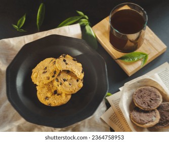 Cookies with raisins and chocolate cookies on black vintage background and beige fabric.
Cookies accompanied by a cup of coffee and decorated with leaves and book pages - Shutterstock ID 2364758953