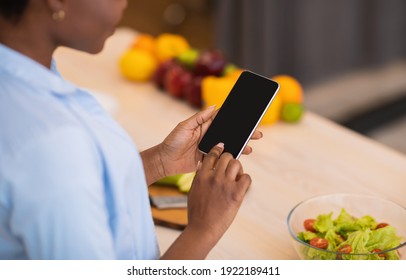 Cooking App. Unrecognizable African Lady Using Phone With Empty Screen Preparing Dinner Standing In Modern Kitchen At Home. Weight Loss Mobile Application For Cellphone Concept. Mockup, Cropped