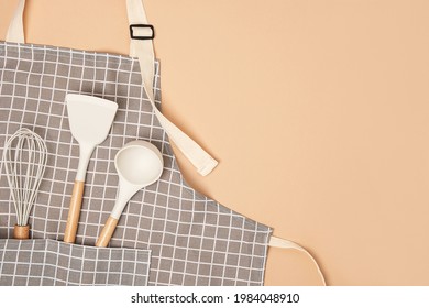 Cooking background. Flat kitchen accessories. Apron and silicone cooking utensil with wooden handle on beige background with copy space. Top view Flat lay.