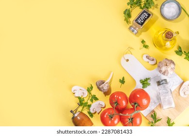 Cooking background with vegetable ingredients. Healthy dinner preparation flat lay, with fresh raw tomatoes, onion, garlic, herbs and greens, olive oil, salt, pepper seasonings, on yellow background 