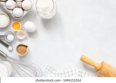 Cooking And Baking Ingredients Utensils On White Concrete Background. Kitchen Food Frame. Eggs Sugar Milk Whisker Rolling Pin And Measuring Spoons With Spices