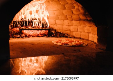 A cooking and baking pizza in a firewood oven. Pizza Margherita, four cheese or meat pizza into the oven. Italian traditional pizza is cooked in a stone wood-fired oven. - Shutterstock ID 2173098997
