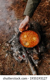 Cooking beans in a pan on bonfire. Man adding eggs to bean sauce. Cooking vegetables on an open fire for family. Making food in camping trip. Active adventurous lifestyle in balance with the nature.