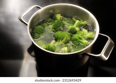Cooking broccoli in boiling water in a stainless steel pot on the black cooktop in the kitchen, preparation for a healthy vegetable meal, copy space, selected focus, narrow depth of field