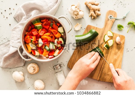 Cooking - chef's hands preparing vegetable vegetarian stew (thick soup). Kitchen scenery - pot with recipe ingredients around on the grey stone worktop captured from above (top view, flat lay). 
