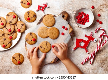Cooking Christmas gingerbread.  Child's hand decorating red nosed reindeer cookies with chocolate buttons and melted chocolate. Festive homemade decorated sweets