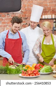 Cooking Class, Culinary, Food And People Concept - Happy Couple And Male Chef Cook Cooking In Kitchen