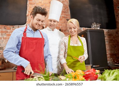 Cooking Class, Culinary, Food And People Concept - Happy Couple And Male Chef Cook Cooking In Kitchen