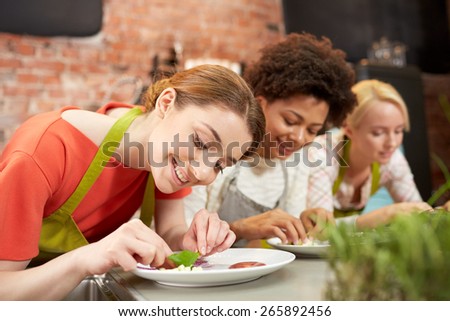cooking class, friendship, food and people concept - happy women cooking and decorating plates with dishes in kitchen