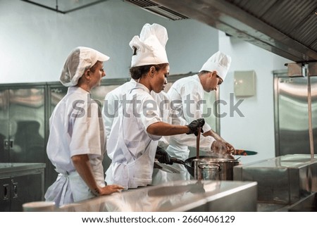 Cooking class in session. Diverse culinary student receiving hands-on training from head chef in a busy restaurant kitchen with focus and dedication.