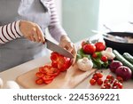 Cooking concept. Unrecognizable woman in grey apron making healthy dinner, cropped of lady preparing delicious meal at home, cutting vegetables on chopping board, kitchen interior, closeup