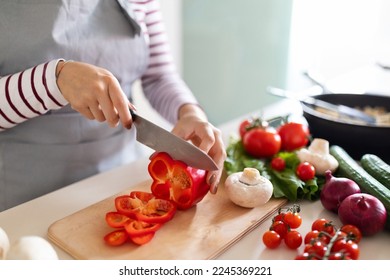 Cooking concept. Unrecognizable woman in grey apron making healthy dinner, cropped of lady preparing delicious meal at home, cutting vegetables on chopping board, kitchen interior, closeup - Shutterstock ID 2245369221