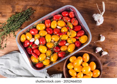Cooking confit of multi-colored cherry tomatoes with garlic, hot pepper and thyme on the table with ingredients, top view in a baking sheet