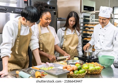 Cooking  Course , Senior Asian Male Chef In Cook Uniform Teaches Young Asian And African American People Cooking Class Students To Prepare, Mix Ingredients For Pastry Foods, Fruit Pies In Restaurant .