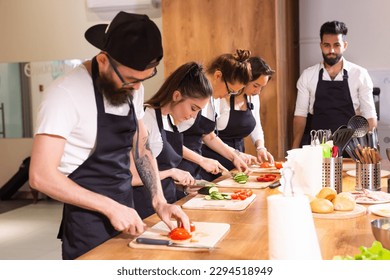 Cooking course - senior male chef in cook uniform teaches young people cooking class students to prepare and mix ingredients for dishes in restaurant kitchen - Powered by Shutterstock