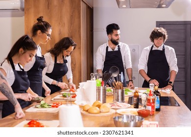 Cooking course - senior male chef in cook uniform teaches young people cooking class students to prepare and mix ingredients for dishes in restaurant kitchen - Powered by Shutterstock