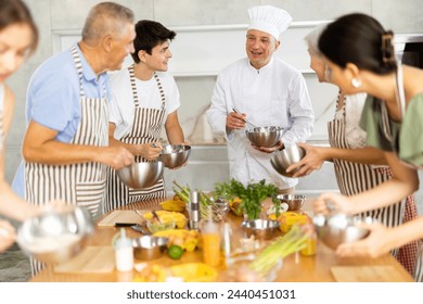 Cooking course - senior male chef in cook uniform teaches young people cooking class students to prepare and mix ingredients for dishes in restaurant kitchen - Powered by Shutterstock