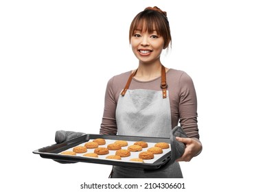 cooking, culinary and bakery concept - happy smiling female chef or baker in apron holding baking tray with oatmeal cookies over white background - Powered by Shutterstock