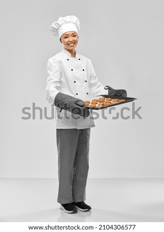 cooking, culinary and bakery concept - happy smiling female chef or baker in toque holding baking tray with oatmeal cookies over grey background