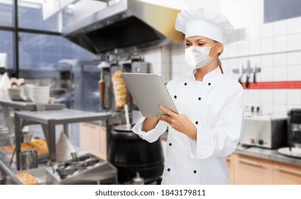 Cooking, Culinary And Health Concept - Female Chef In Toque Wearing Face Protective Medical Mask For Protection From Virus Disease With Tablet Pc Computer Over Kebab Shop Kitchen Background