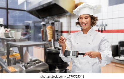 cooking, culinary and people concept - happy smiling female chef in toque with saucepan over restaurant or kebab shop kitchen background