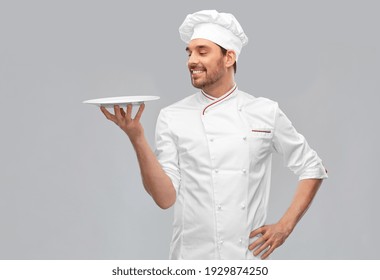 cooking, culinary and people concept - happy smiling male chef in toque holding empty plate over grey background