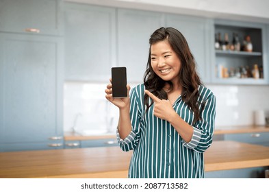 Cooking, Culinary And People Concept - Happy Asian Young Woman With Smartphone Over Kitchen Background