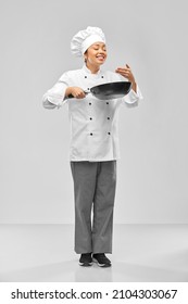 cooking, culinary and people concept - happy smiling female chef with frying pan smelling food over grey background