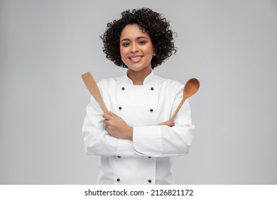 cocina, cocina y concepto de la gente - chef sonriente feliz con chaqueta blanca con cuchara de madera y espátula sobre fondo gris